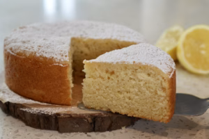 Slice of vegan lemon ricotta cake showing soft crumb, with lemon in background