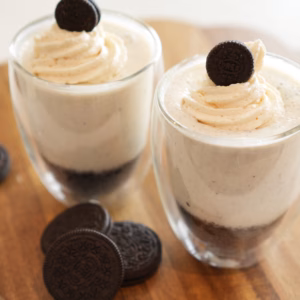 No-bake vegan cookies and cream cheesecake mugs topped with Oreo cookies