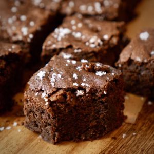 Fudgy vegan brownies with flaky sea salt on a wooden board
