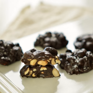 Split chocolate peanut cluster showing roasted peanuts inside, with whole clusters behind it.