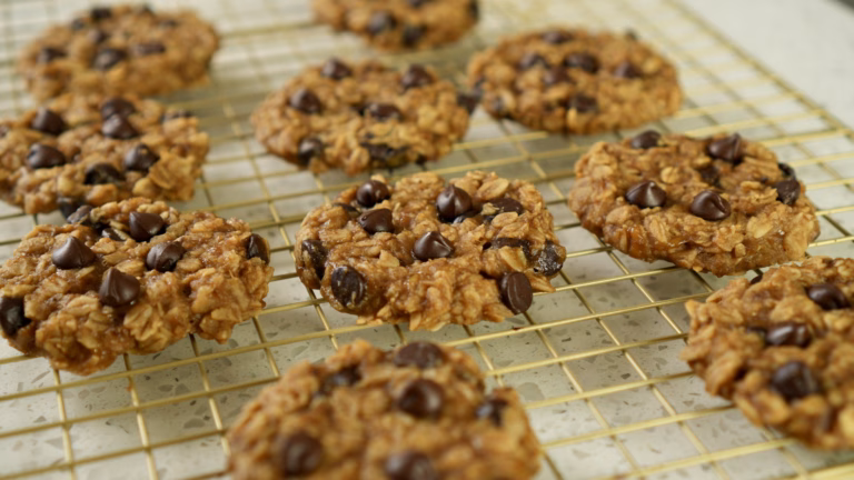 Banana oat cookies with chocolate chips arranged on a gold-coloured cooling rack.