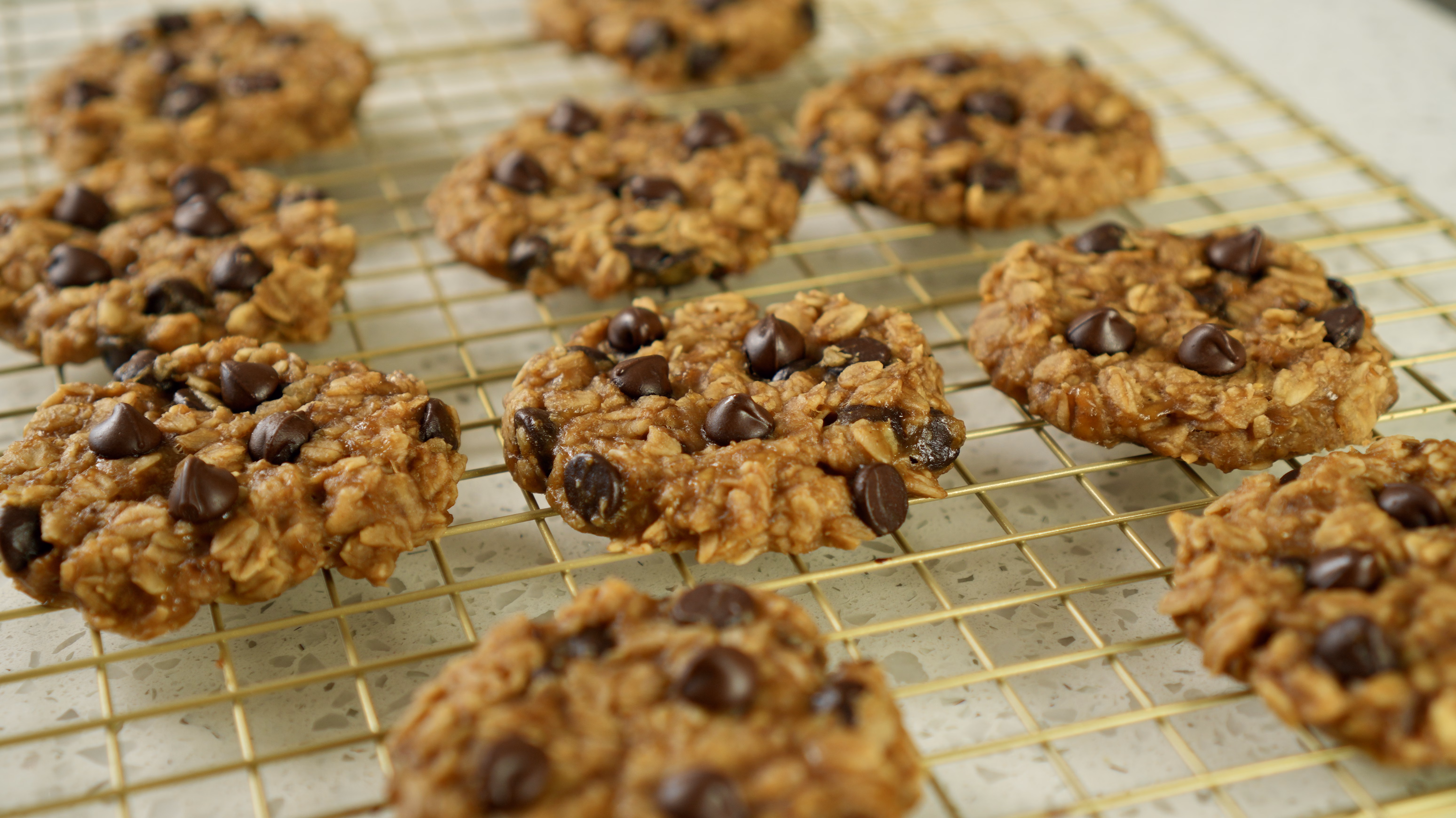 Banana oat cookies with chocolate chips arranged on a gold-coloured cooling rack.