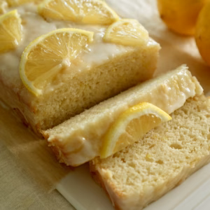 Sliced lemon loaf cake with white icing and lemon slices, showing the fine crumb inside.