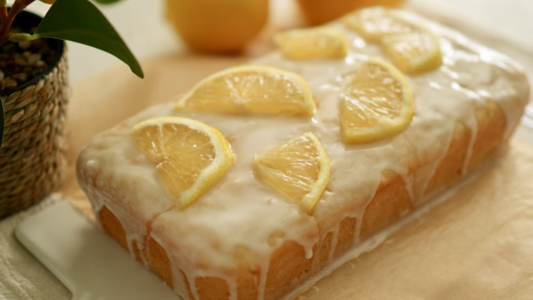 Lemon loaf cake covered with white icing and thin lemon slices on a white serving platter.