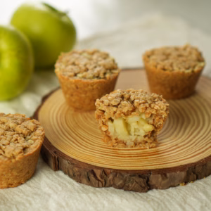 Apple oat cup cut open to reveal diced apples beneath a crumbly oat topping, with whole cups behind it.
