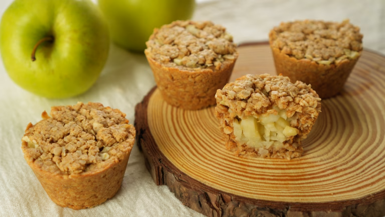 Four golden apple oat cups beside green apples, with one cut open to show the diced apple filling.