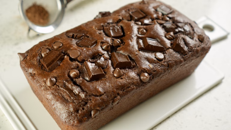 Chocolate loaf cake topped with chocolate chips and large chocolate chunks on a white serving platter.