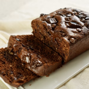 Sliced chocolate loaf cake with chocolate chips in the crumb and chocolate chunks on top, on a white platter.