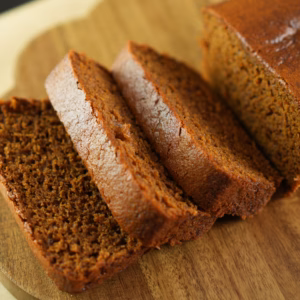 Sliced vegan gingerbread loaf showing its dark crumb on a wooden board