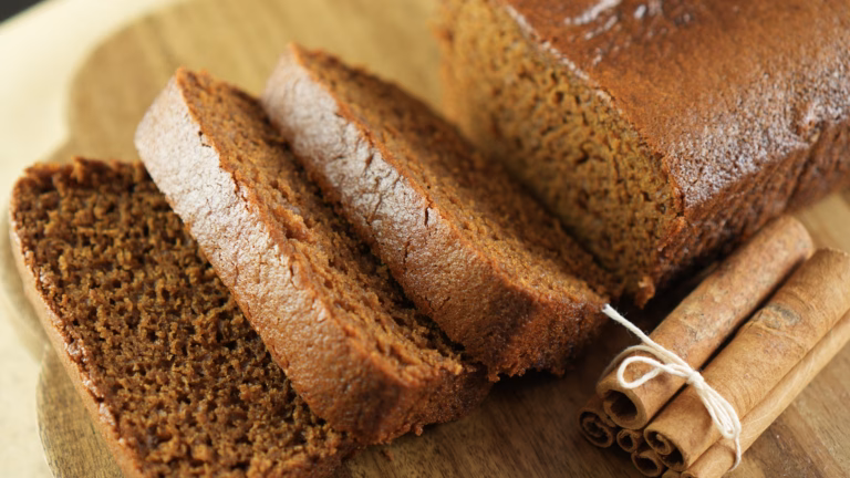 Vegan sticky gingerbread loaf cake with sliced pieces and cinnamon sticks on a wooden board